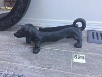 Side view of black cast iron dachshund door weight showing detailed head, legs, curled tail, and elongated body.