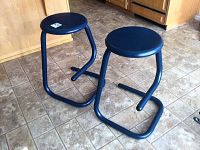 Two blue metal stools displayed on a tiled floor showing the overall shape and construction.