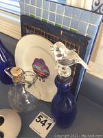 Blue and clear glass bottles, decorative plate with lips design, and stoneware item with bird design.