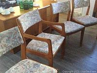 Four teak dining chairs arranged in a row, three armless and one with arms visible; shows overall style, upholstery, and wood finish.