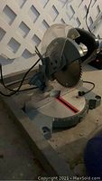 Delta miter saw shown from side with metal base, circular blade, and clear blade guard.