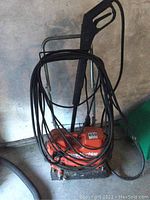 Full view of Coleman Clean Machine 1200 pressure washer with hoses wrapped around the handle, showing orange body and metal frame.