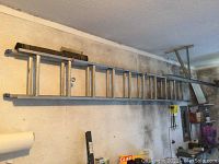 Long view of the aluminum ladder mounted horizontally on a wall in a garage or workshop area.