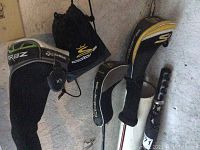 Multiple Cobra headcovers and a TaylorMade RBZ headcover hanging on rail with clubs in background