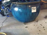 Large blue pottery ceramic pot shown from side, showcasing rounded shape and glazed blue finish with a slightly greenish rim.