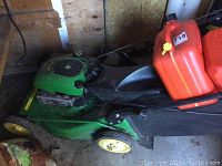 Side view of green mower with two red jerry cans strapped