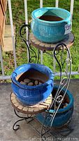 Full view of black metal stand holding three round ceramic garden pots in turquoise, blue, and teal colors, showing tiered design and tile platforms.