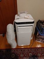 Front view of white UberHaus portable air conditioner with attached flexible exhaust hose.