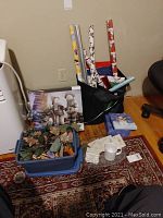Photo showing rolls of Christmas wrapping paper in a black bag and other holiday items on a red patterned rug.