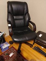 Black leather swivel office chair with wooden armrests and caster wheels. Visible stain and scratches on the seat.