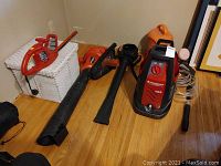 Full view of all items including leaf blower, hedge trimmer, power washer, watering can, and wicker hamper on wooden floor.