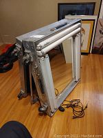 Full view of folded portable lighted makeup center with rectangular mirror and light tubes on top and sides of the frame, placed on a wooden floor.