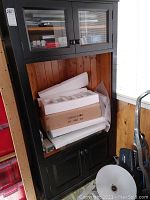Full view of tall wood cabinet with glass paneled double doors on top and solid doors below. Items stored inside bottom section.