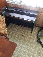 Full view of black Tango electric organ showing its wooden frame, three pedals, and part of a room interior