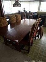 Solid wood rectangular dining table with 6 upholstered chairs in floral fabric, table and chairs shown from perspective view with overall wear and one broken chair visible.