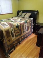 Full view of the bed showing the patchwork quilt bedding, pillows, and the dark wood sleigh frame with leather inlay headboard.