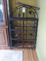 Metal wine rack with decorative grape leaves and clusters, displaying scratches and rust spots.