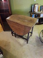 Front-angle view of the closed oval gate leg table showing the twisted wooden legs and table top surface with scratches.