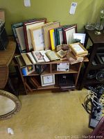 A shelf with multiple assorted picture frames stacked and photo albums placed on and inside the shelf.