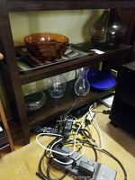 Shelf with amber glass fruit bowl, clear glass bowls and vase, blue plate visible, cables below shelf.