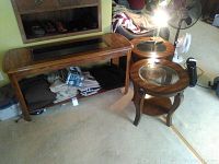 Full view of the wood and glass rectangular coffee table and two matching round end tables placed on carpeted floor.