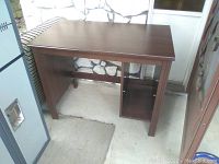 Full view of particle board desk with dark wood finish, rectangular top, and open side compartment missing shelving inserts