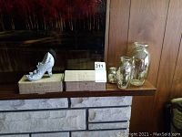 Three mercury glass vases with reflective antique silver finish and two boxes containing Toland wind chimes. Decorative ceramic high heel shoe displayed on mantel shelf.