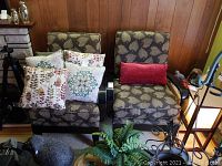 Two matching wooden armchairs with leaf-patterned upholstered cushions, accompanied by several decorative throw pillows.