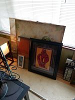 Multiple wall art pieces leaning against window sill including framed and unframed items.