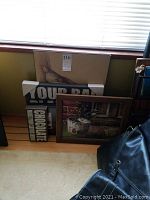 Wall art pieces leaning against wall under window, showing multiple framed and cardboard backed pieces with bird imagery and text