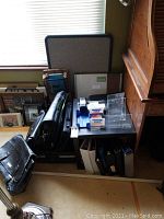 Photo showing black briefcases, binders in various colors, cork message board, clear message board, and a small black table.