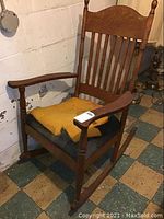 Full view of wooden rocking chair showing torn yellow seat cushion and overall wear.