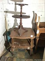 Photo of two vintage wooden tables stacked: a three-tier stand with round tiers and turned column above a square side table with curved legs and aprons, visible mildew on surfaces.