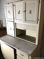 Front view of vintage white metal kitchen cabinet showing multiple storage doors and open bread box section with roll-top door.
