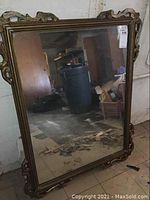 Full view of rectangular vintage mirror showing ornate wooden frame with gold-tone finish and aged mirror glass, placed in basement setting.