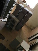 Various stacks of gray concrete cinder blocks arranged inside a basement area on tiled floor.