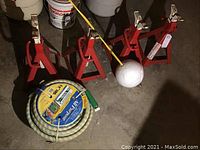 Four red American Forge garage stands arranged on the floor with garden hose reel placed in front. Items are heavy and made for automotive use.