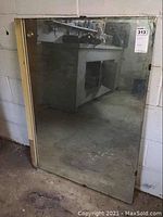 Full view of large rectangular mirror standing against a wall in a basement space. Mirror has visible spots and a wooden frame with corner brackets.