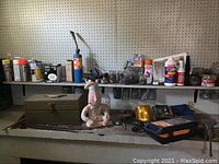Shelf with toolbox, spray cans, hardware items, figurine, tools, and container with sticks or matches.