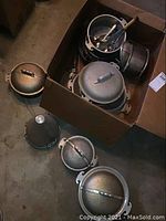 Photo showing multiple Guardian pots with domed lids and some pots without lids in a box, along with flatware and a metal sifter.