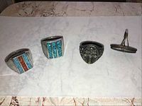 Four rings with turquoise and coral chip inlay and intricate designs laid flat on marble surface