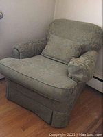 Full view of upholstered armchair with floral pattern fabric and matching throw pillow on wooden floor near wall.