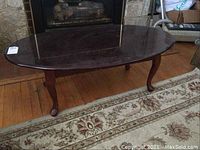 Full view of the oval wooden coffee table on a patterned rug showing scratched surface.