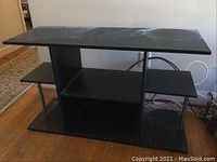 Full front view of black TV stand showing top surface, center shelves, and side platforms for additional storage.