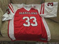 Full front of red and white Maryland Terps football jersey laid flat on couch, showing number 33 on chest and sleeves.