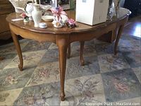 Full view of wooden Thomasville dining table showing curved edges and several decorative items on top.