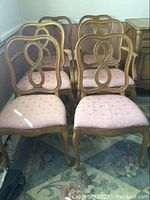 Overall view of six wooden dining chairs, including two captain's chairs at the back and four regular chairs in front, arranged on a floral rug.