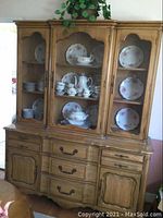 Full view of the wooden china hutch showing three glass doors on top containing porcelain dish set and wooden drawers and cabinets below.
