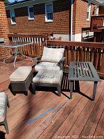 Full view of the outdoor lounge chair with soiled cushions, ottoman, woven ottomans and coffee table on wooden deck.