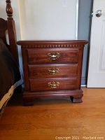 Front view of nightstand showing three drawers with brass handles and carved trim